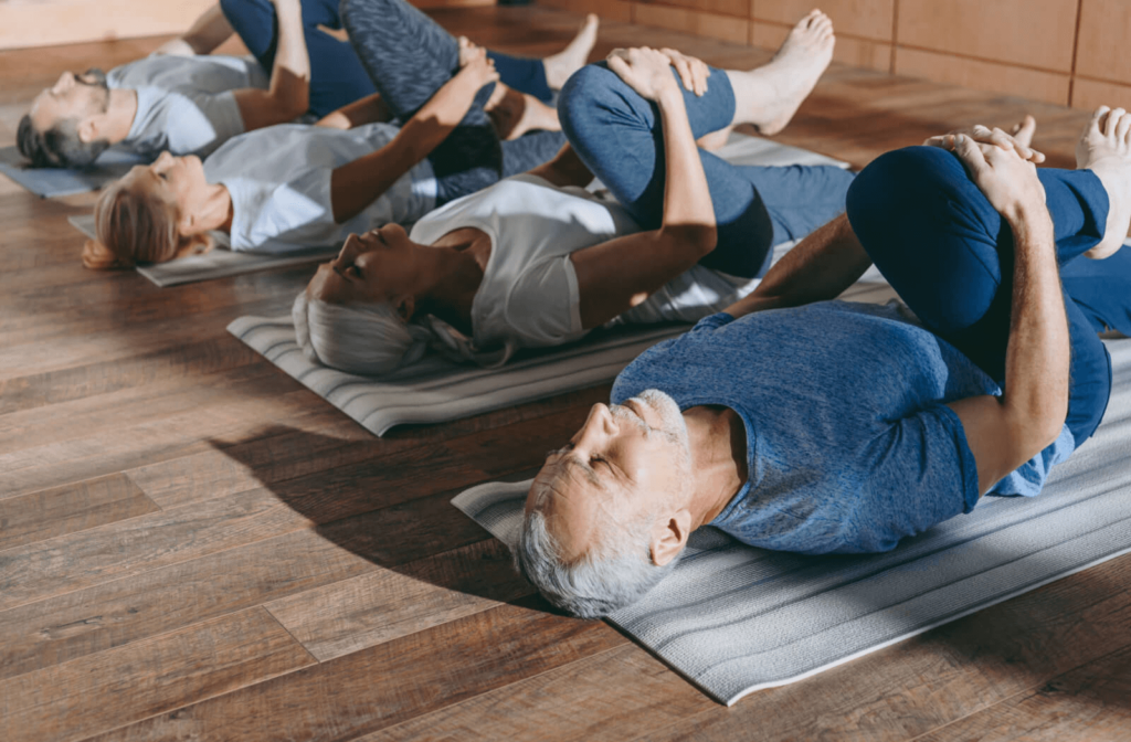 A group of seniors with their backs on an exercise mat stretching their hamstrings.
