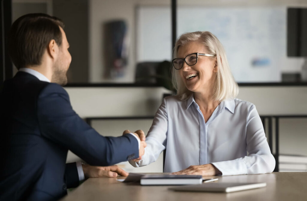 An older adult shaking hands with a young professional after a meeting to plan the start of a senior care business.