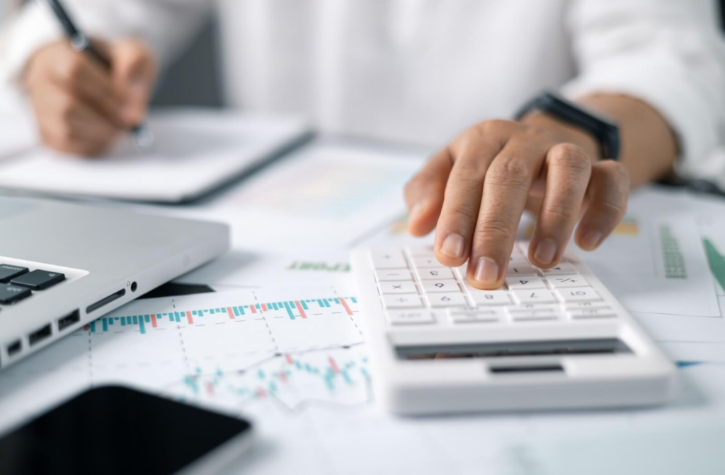 A businessperson is handling finances and calculations on a desk, considering the cost of opening a senior living community.